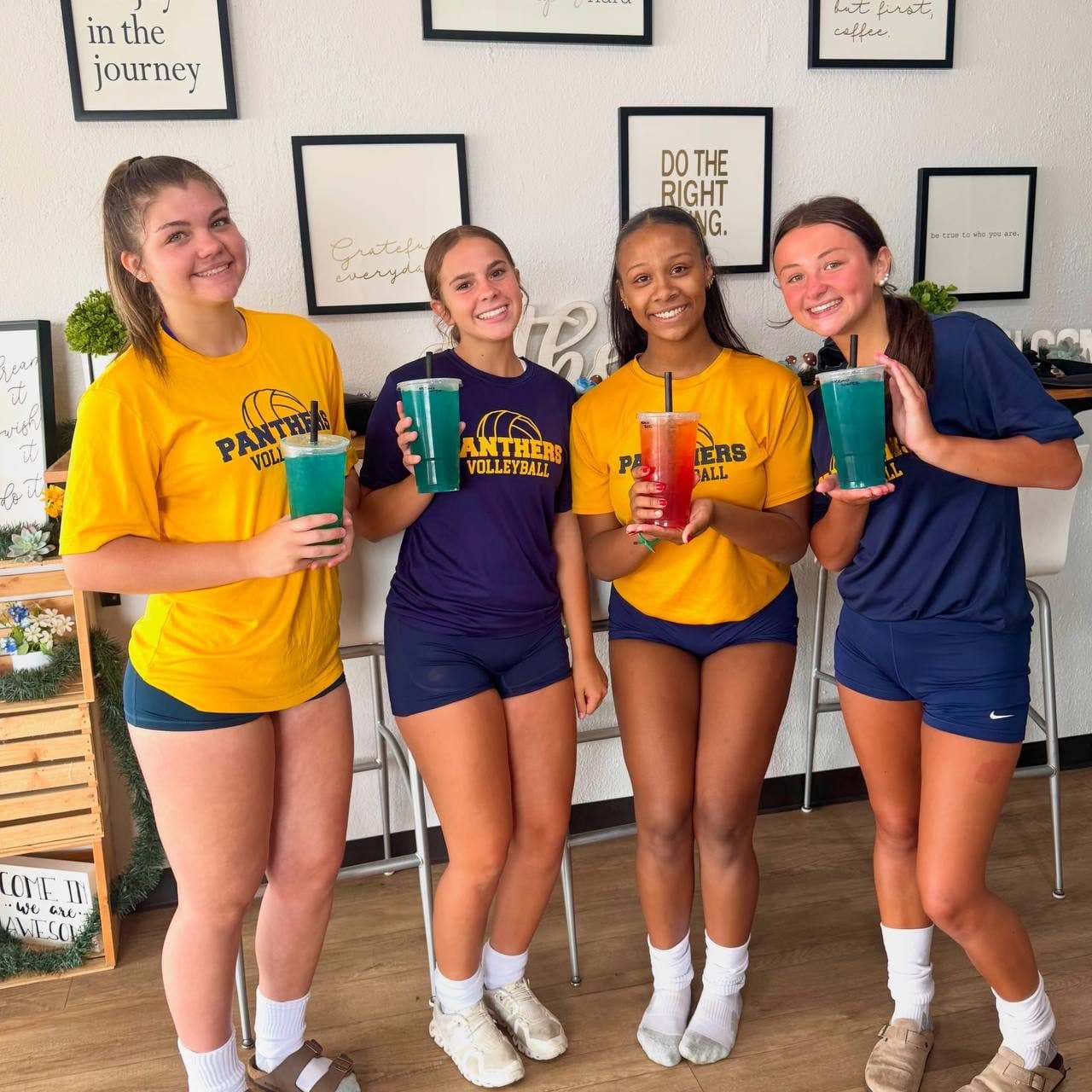 Four volleyball teammates smiling with their loaded teas inside Spartans Nutrition